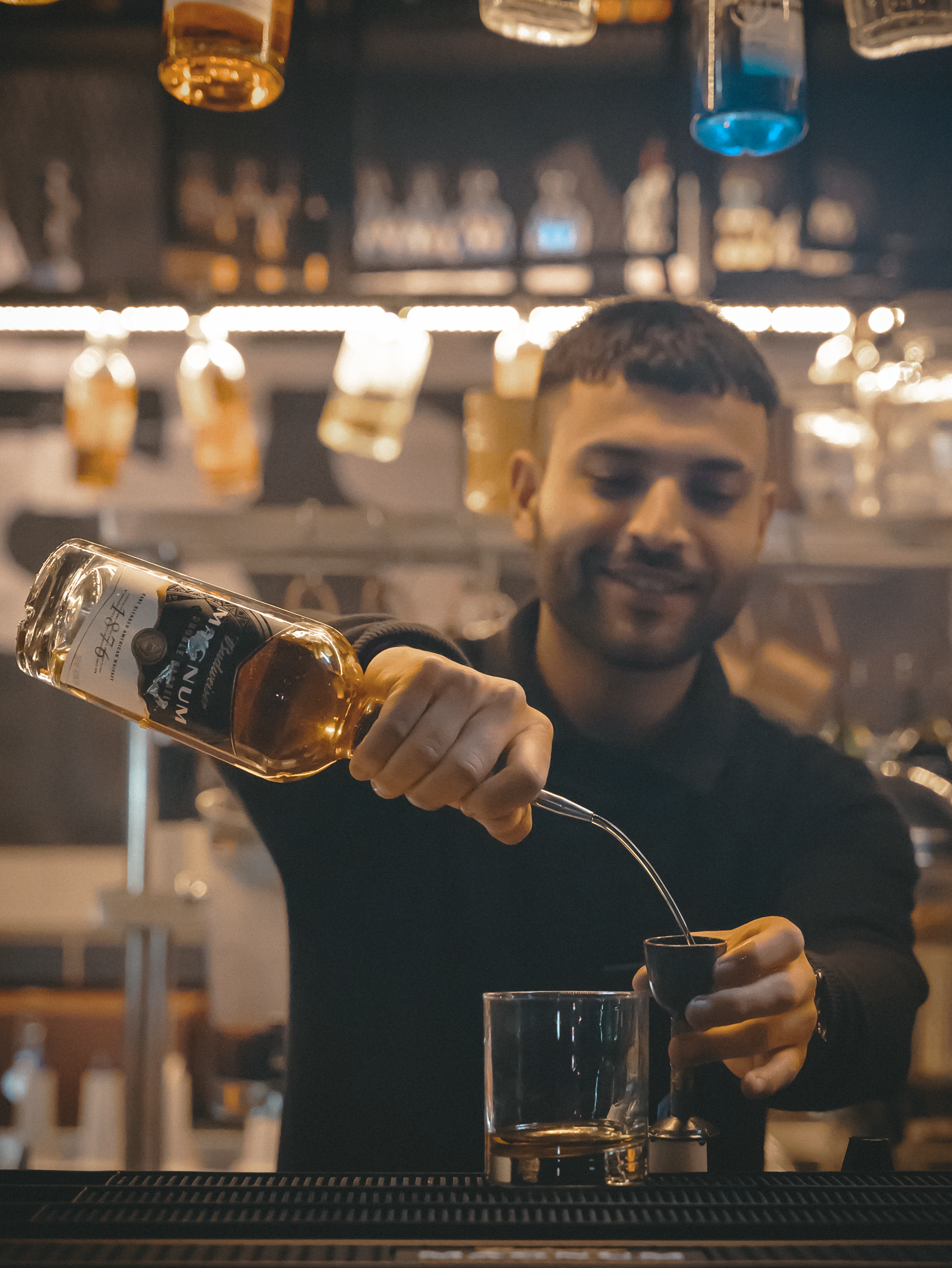Male bartender skillfully pouring whiskey at a modern bar setup.
