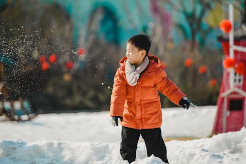 Boy in Orange Jacket Standing on Snow Covered Ground