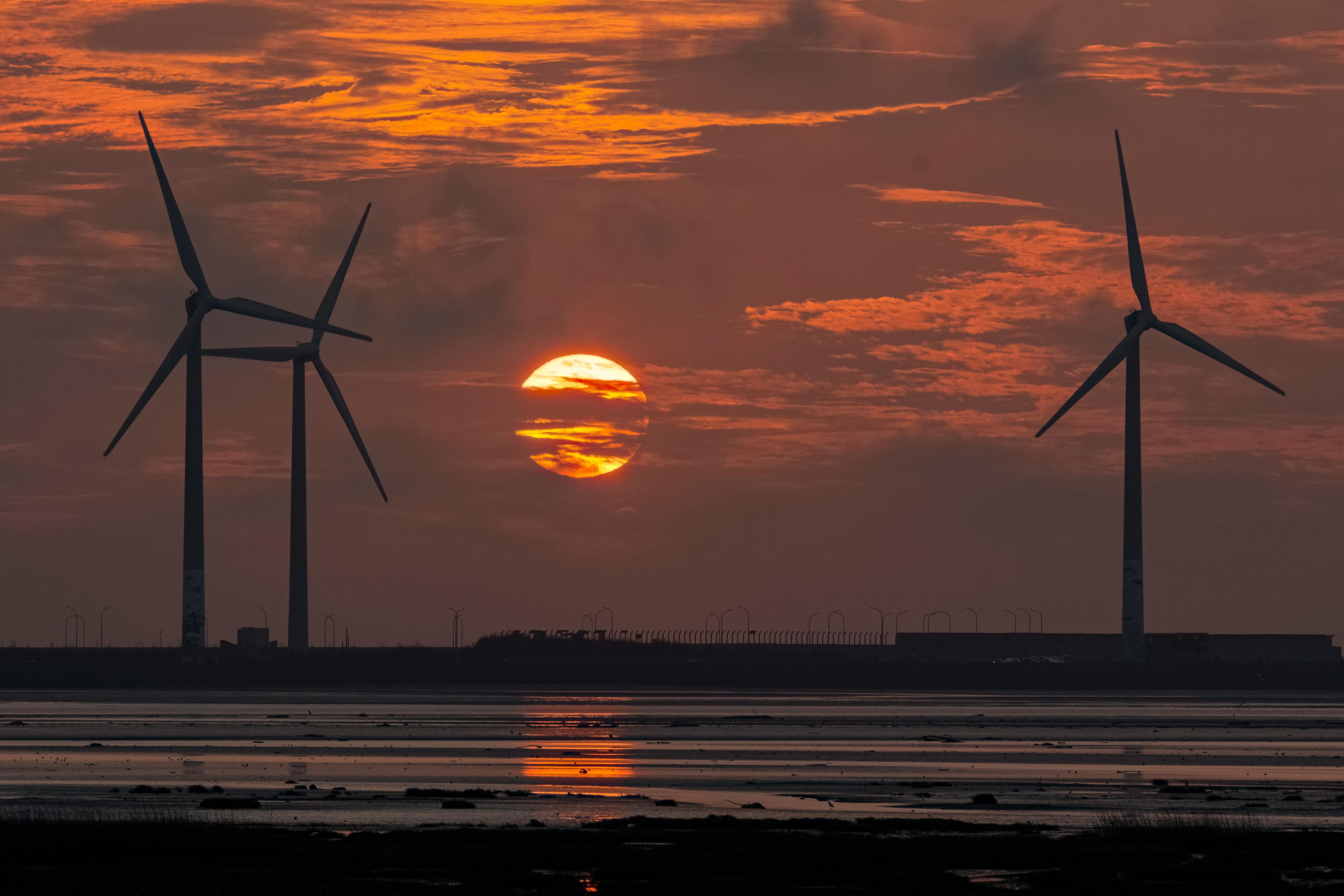 Scenic view of wind turbines silhouetted against a vibrant sunset sky reflecting on water. Ideal for renewable energy themes.