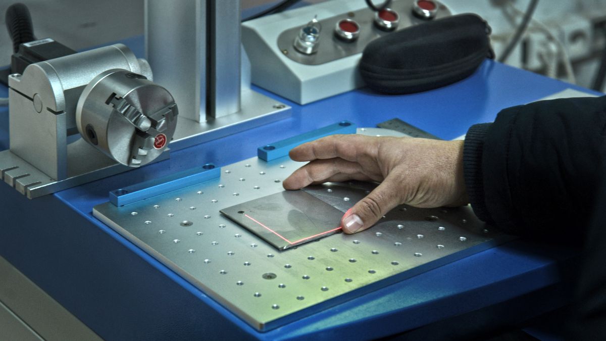 Hand positioning a metal plate under a red laser line in laboratory equipment.