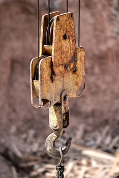 Close-up of a rusty industrial hook and pulley system outdoors in sunlight.