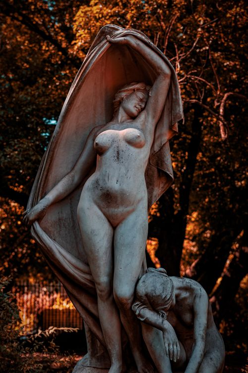 Free Marble sculpture of two figures elegantly posed against an autumn forest backdrop with warm lighting. Stock Photo