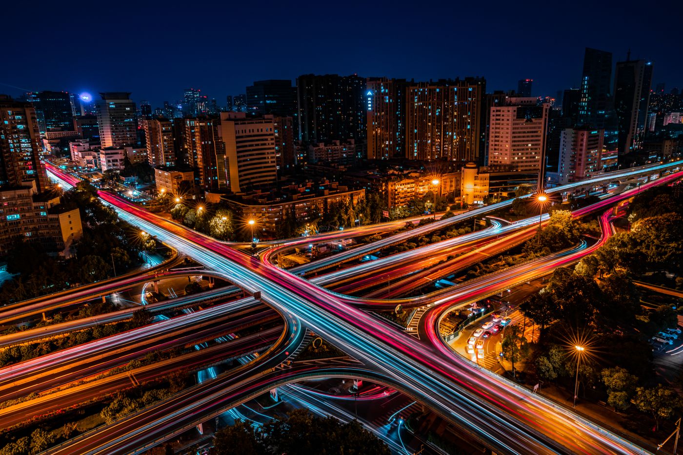 Aerial view of a bustling city intersection with vibrant light trails and illuminated skyscrapers at night.