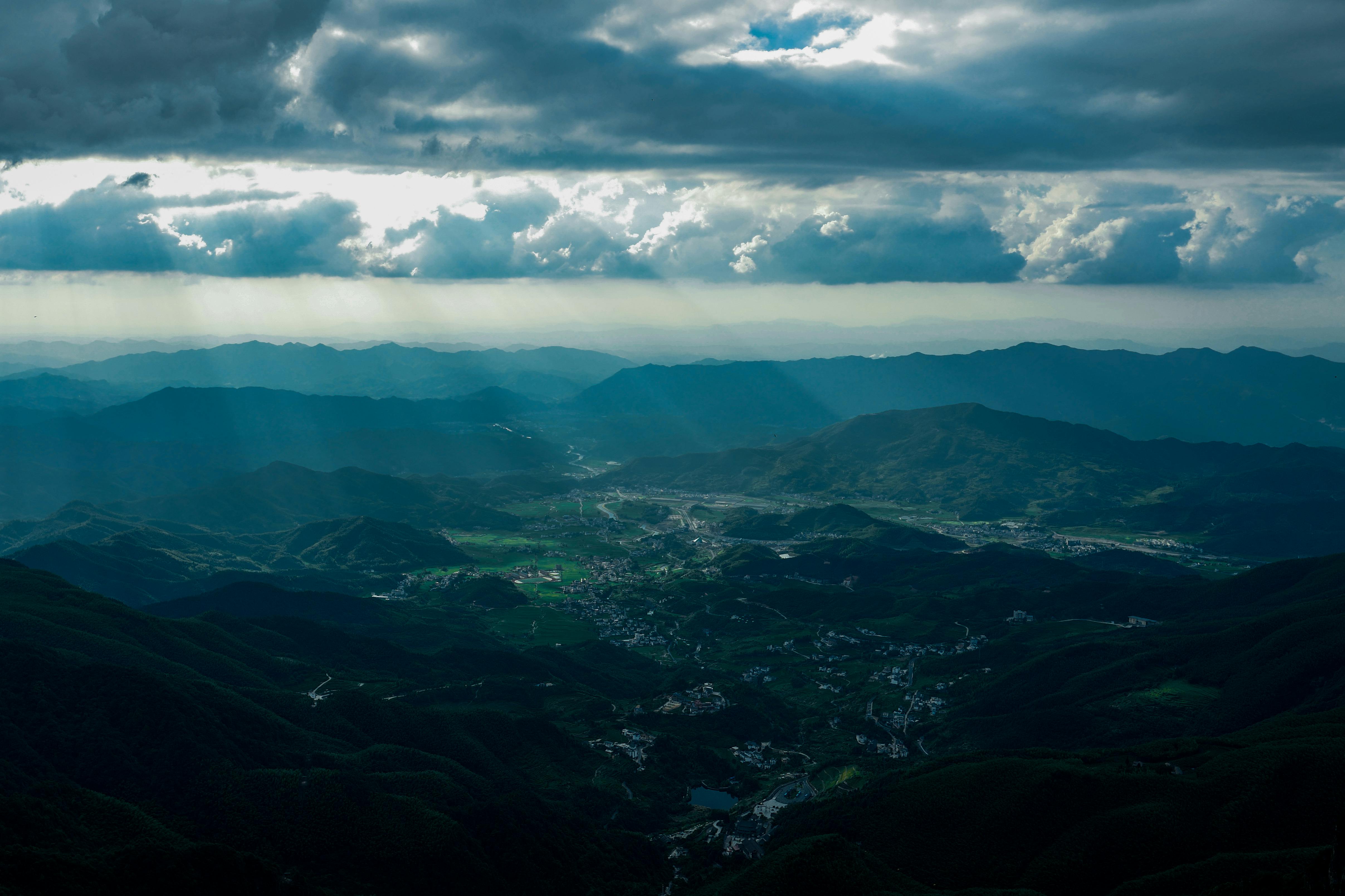 Free A stunning aerial view of a mountainous landscape with valleys and scattered towns underneath a dramatic cloudy sky. Stock Photo