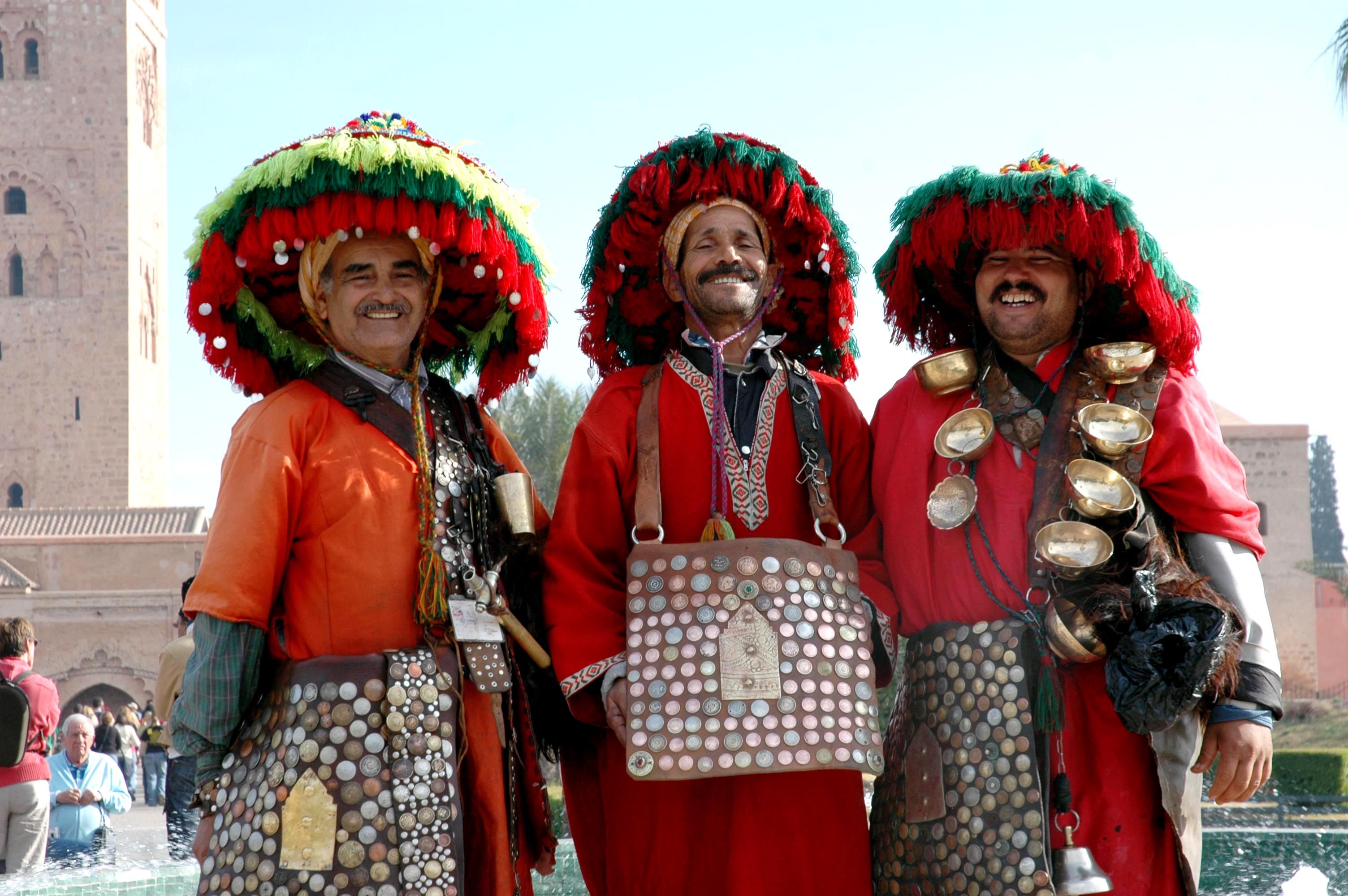 Traditional Berber water sellers in colorful costume and tasseled hats in front of the Koutoubia Mosque in Marrakech, the end point of this tour