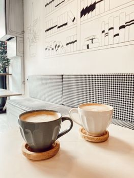 Two stylish coffee cups on a cozy table in a modern café with artistic interior design.
