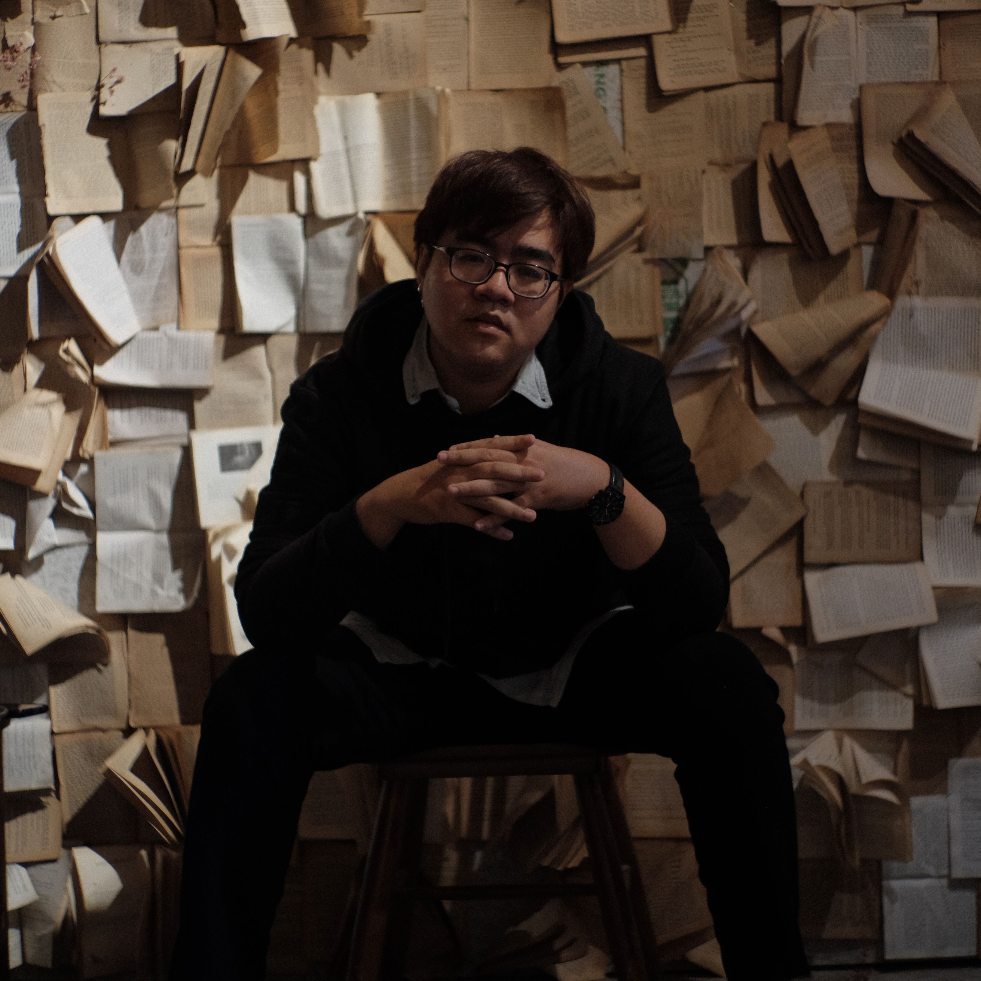 Artistic portrait of a man seated in front of a wall adorned with open books, creating a thoughtful ambiance.
