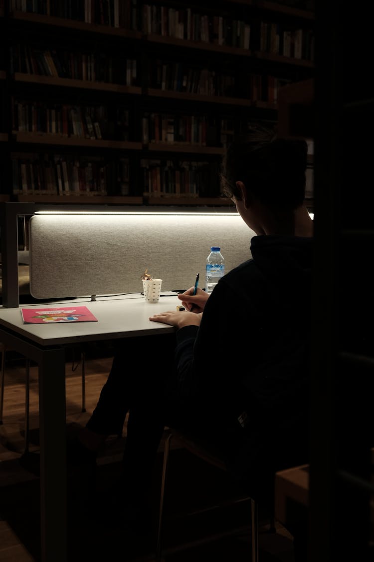 Person Sitting In Darkness By Table And Writing