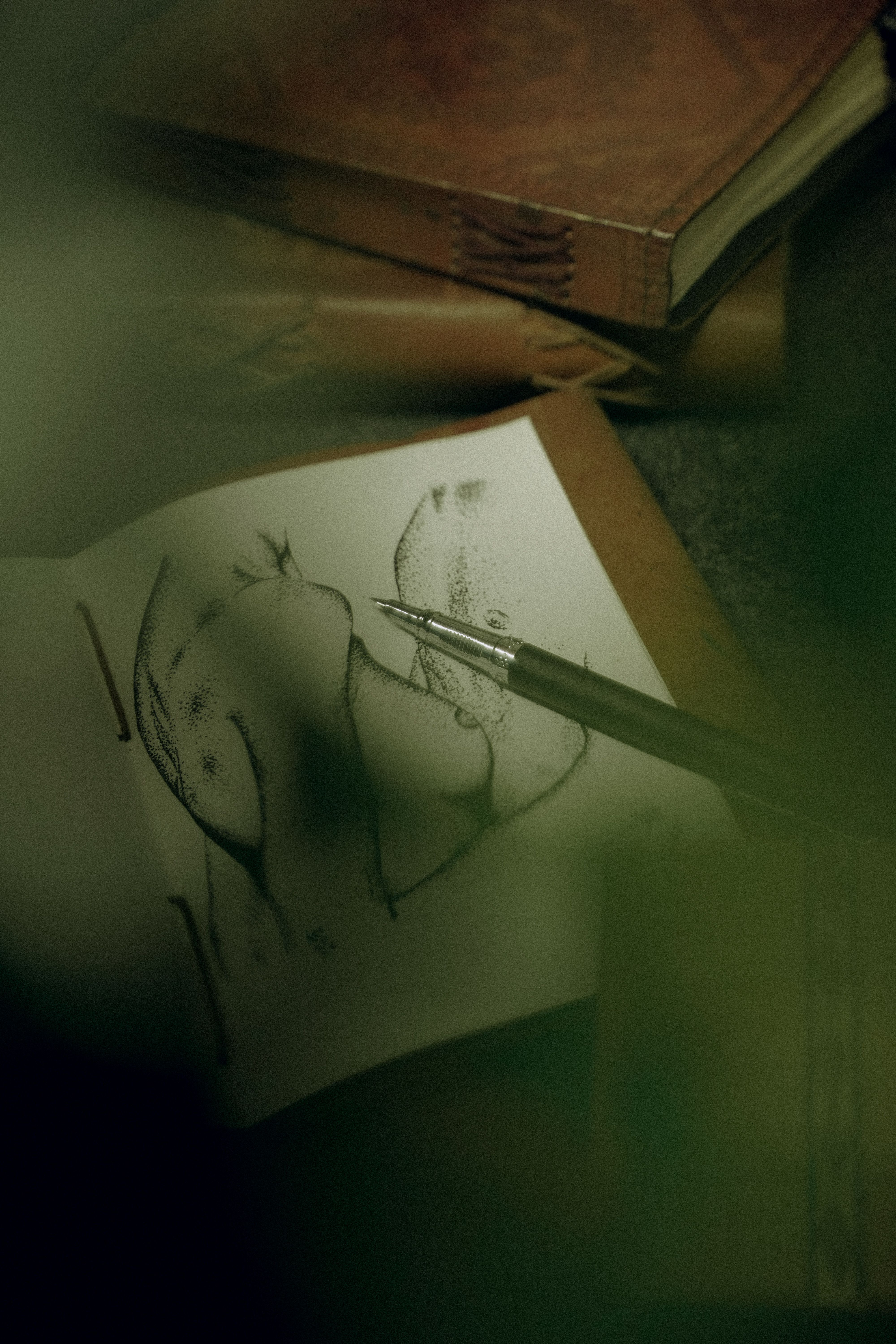 A close-up view of a pen sketching on a notebook surrounded by books, evoking creativity and focus.