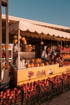 Colorful outdoor fruit stand with various fruits and a vendor under a clear blue sky.