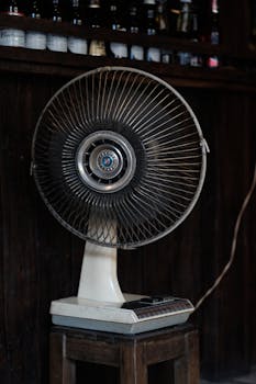 Old-fashioned electric fan sitting on a wooden stool, showcasing retro charm indoors.
