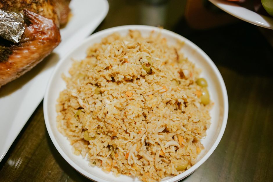 A skillet of Cuban picadillo with ground beef, green olives, and raisins in a red tomato sauce, served over white rice with a lime wedge on the side.