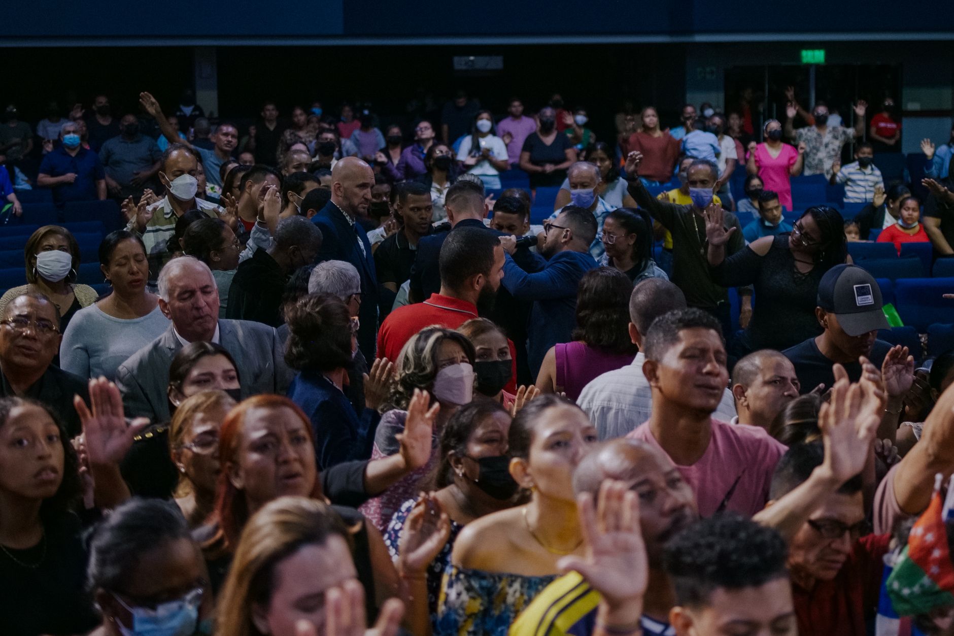 A diverse group of people attending an indoor event, raising hands in participation.