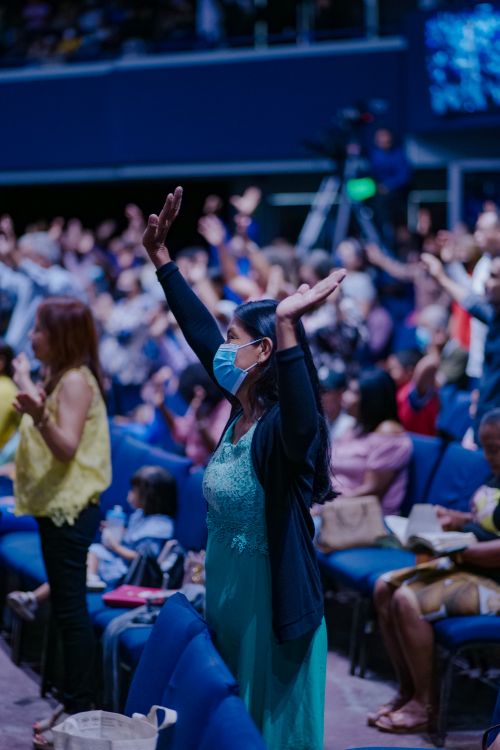 Free A diverse crowd participates in an indoor event with hands raised, highlighting community and engagement. Stock Photo