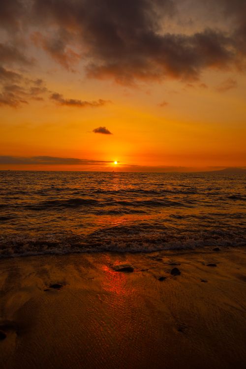 Free A breathtaking sunset over the ocean with golden skies and gentle waves on a sandy beach. Stock Photo