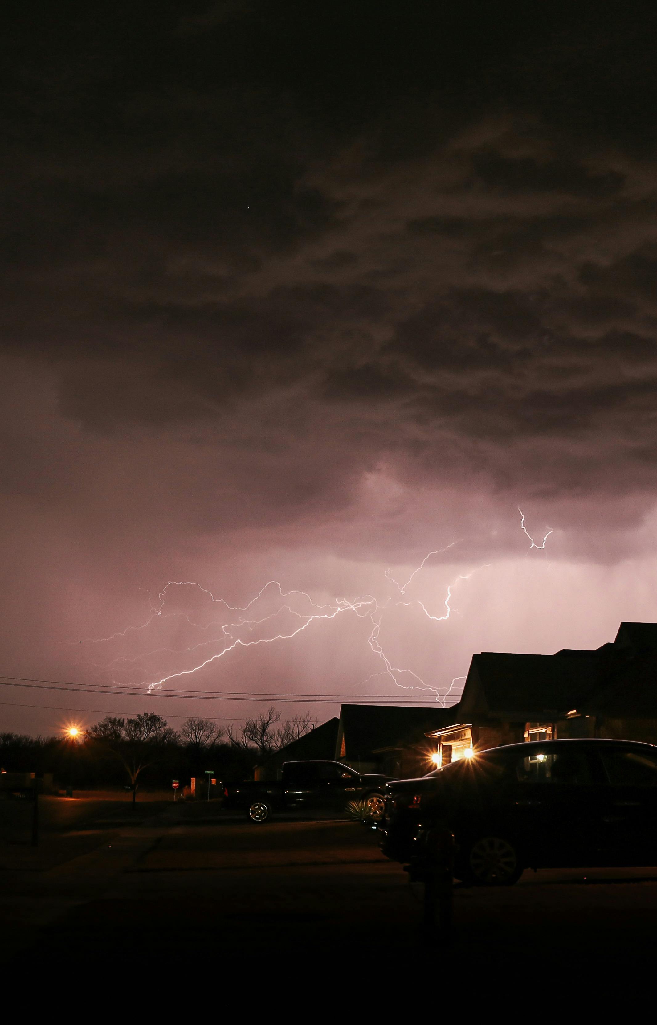 Striking lightning illuminates the night sky over suburban houses, capturing a powerful thunderstorm.
