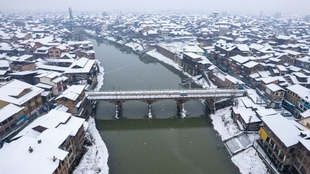 Aerial winter view of a snow-covered bridge over a river in Srinagar, capturing the serene beauty of the landscape.
