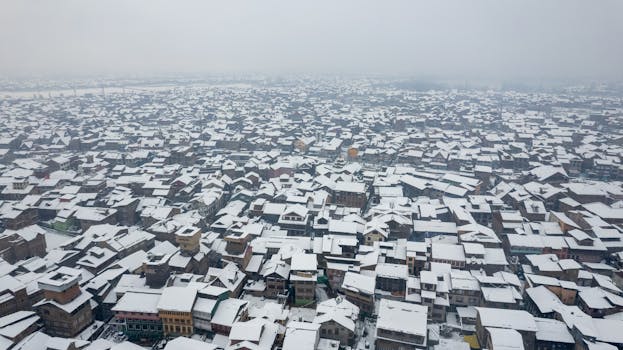 Aerial view over Srinagar city in winter, with snow blanketing the rooftops.
