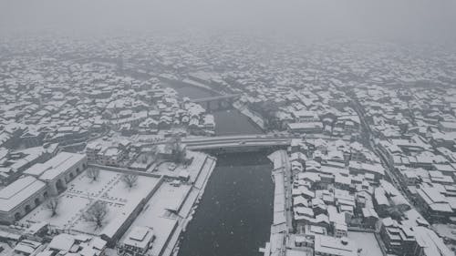 Snowfall over Town with River in Winter