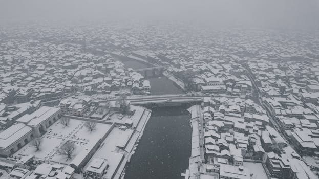 Aerial view of Srinagar in winter with snow-covered buildings and river.