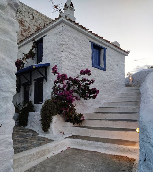 Free Beautiful white stone house adorned with vibrant bougainvillea and blue accents, showcasing rustic Mediterranean architecture. Stock Photo
