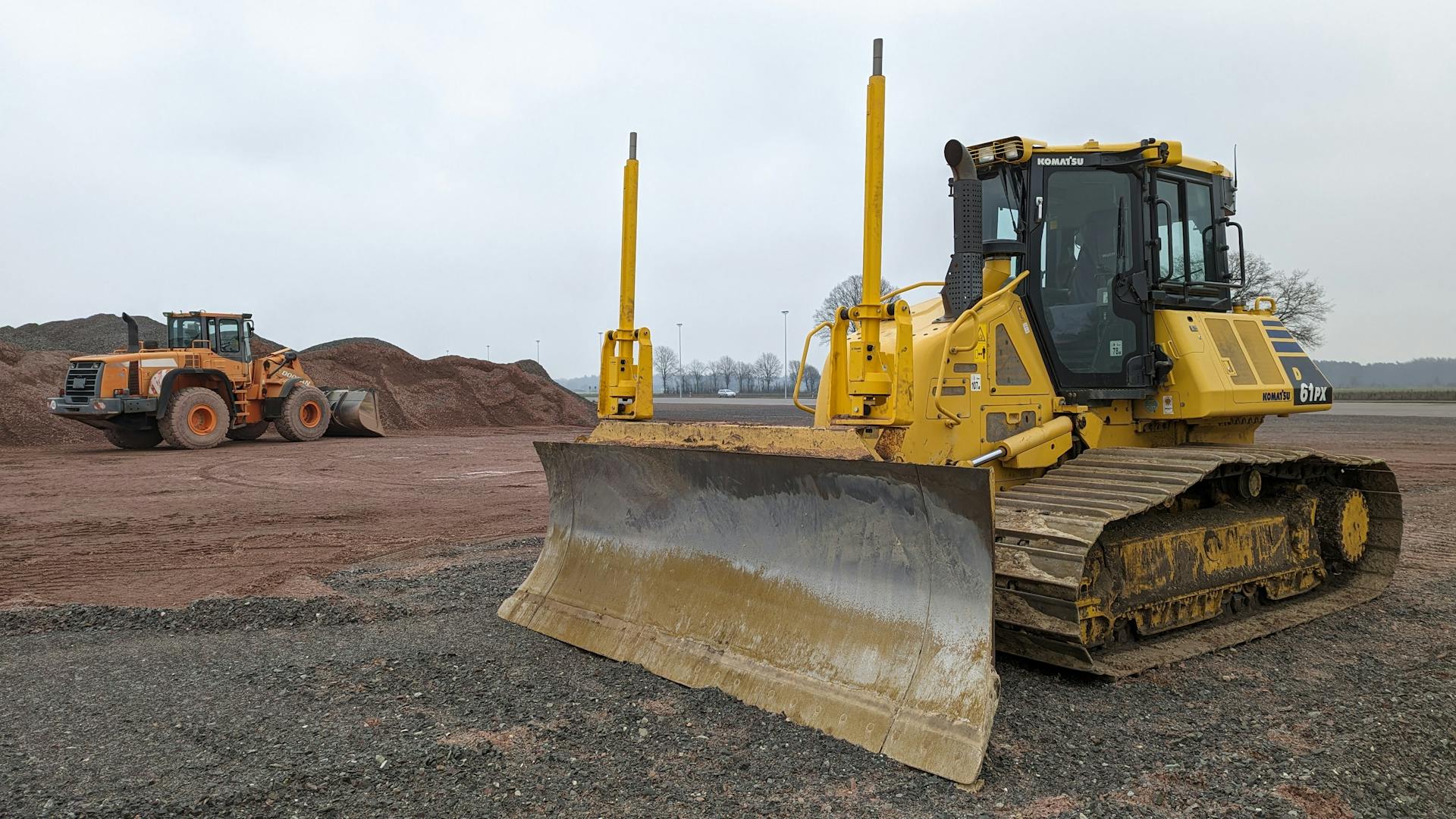 Yellow bulldozer and orange earthmover at Werlte construction site.