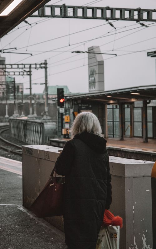 Free Back view of a woman waiting at a Dublin train station platform on a cloudy day. Stock Photo