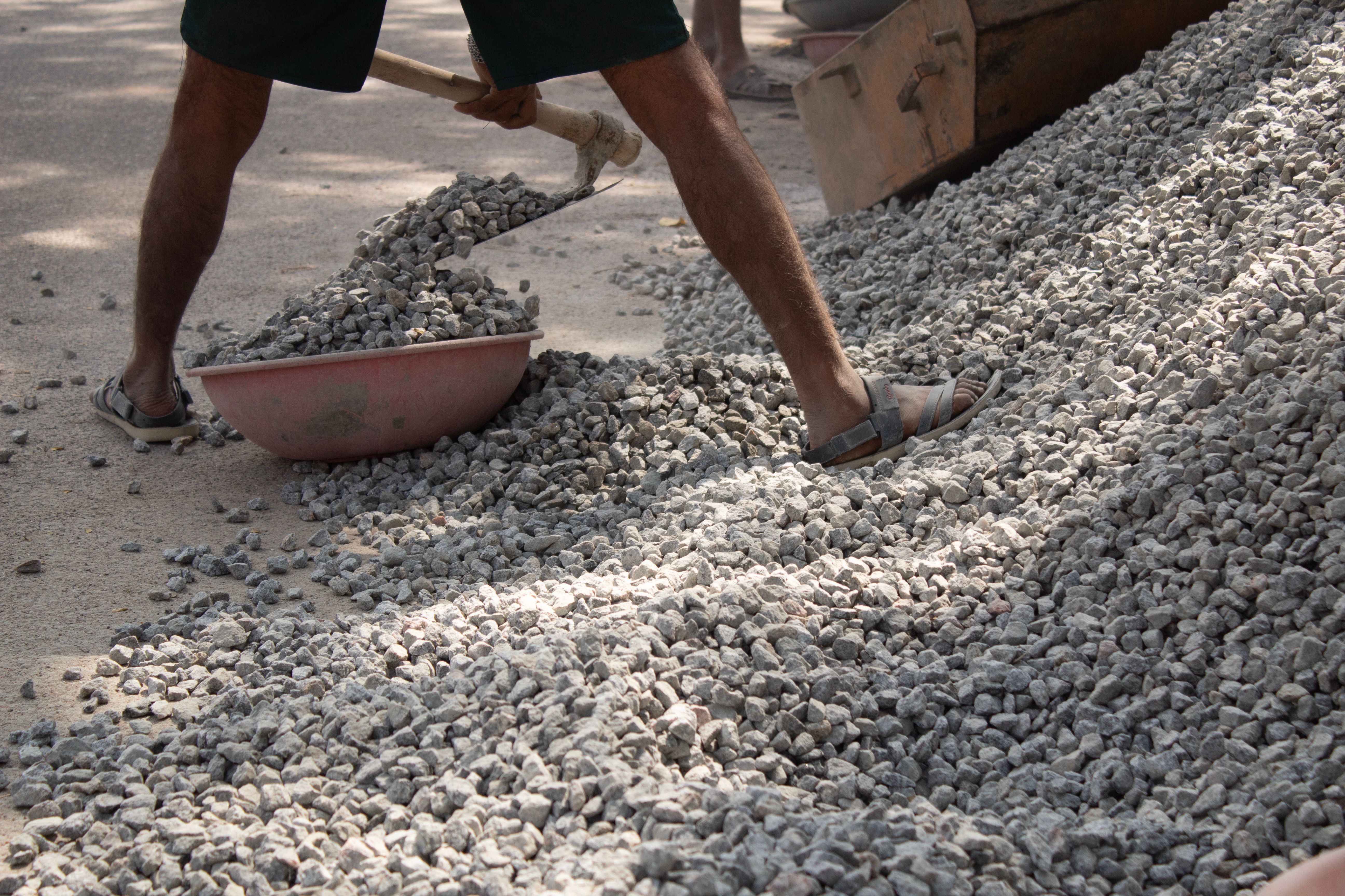 Man using a shovel to move rocks on a construction site in Bengaluru, India. | Indian Village Development