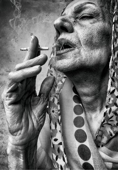Grayscale Photo of an Elderly Woman Smoking a Cigarette