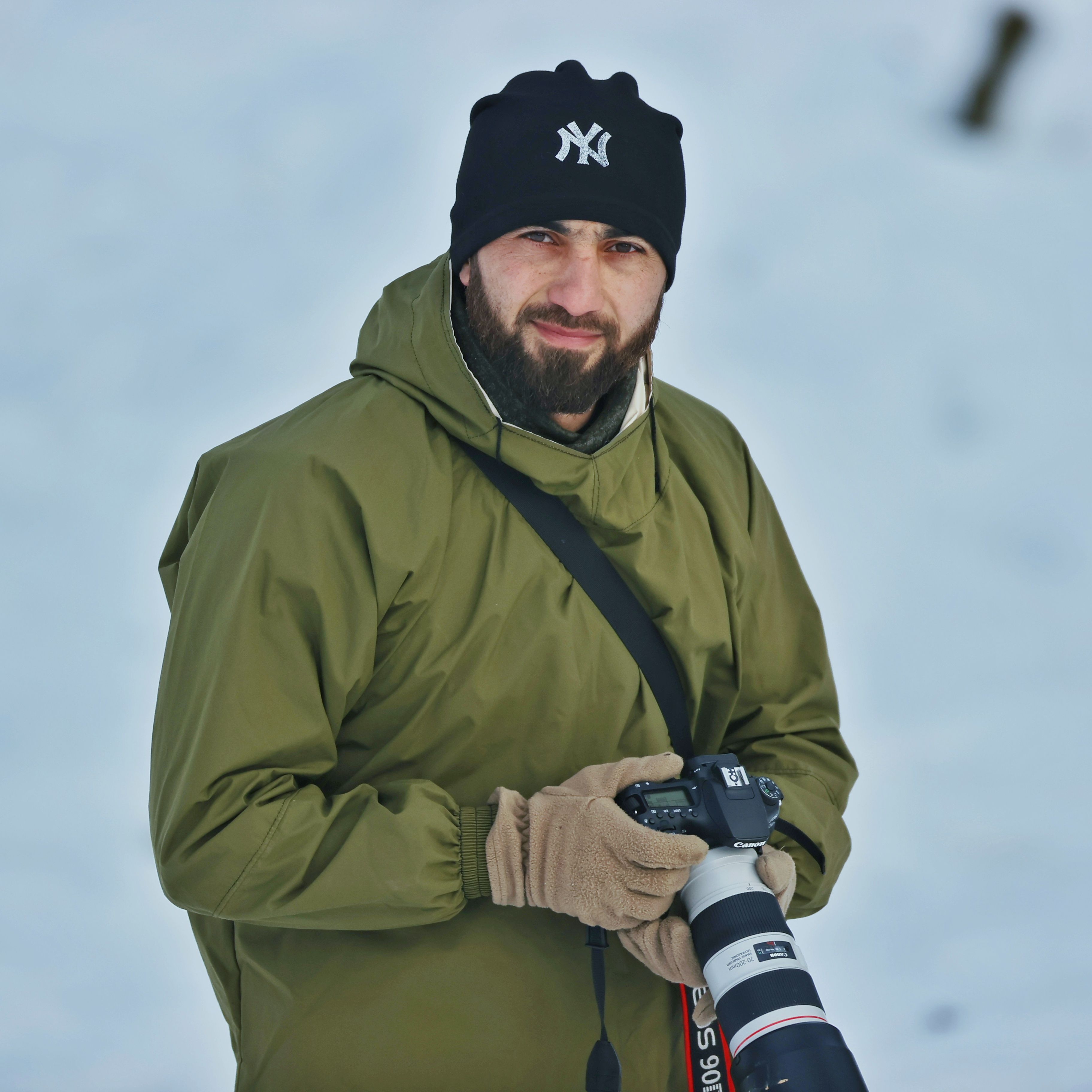 Man in green jacket holds camera in snowy winter scene.