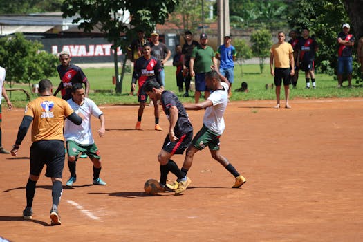 Amateur soccer players in action on an outdoor field under a sunny sky, surrounded by spectators.