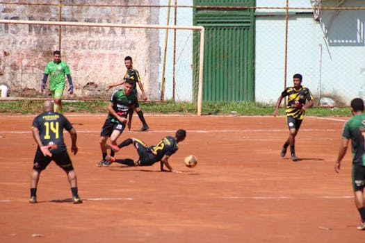 Intense action during an amateur soccer match on a dusty outdoor field.
