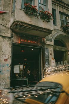 Rustic İstanbul restaurant facade with flowers and blurred taxi passing by.