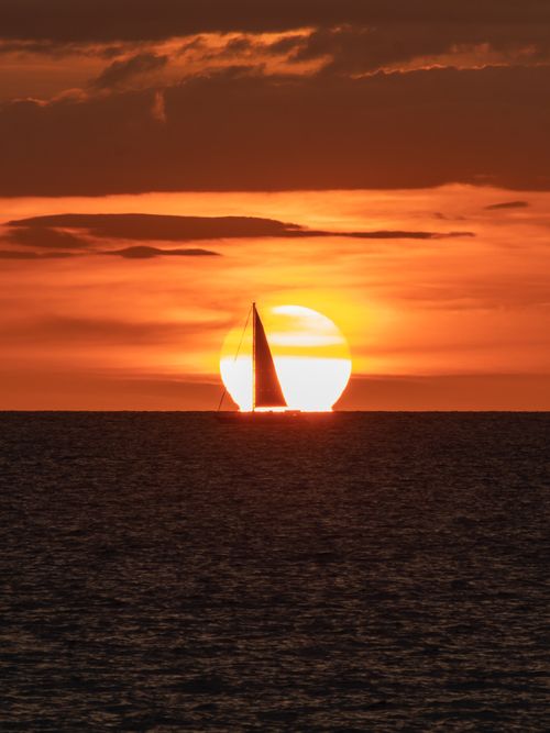 Free A sailboat silhouettes against a vibrant sunset over the sea in Guanacaste, Costa Rica. Stock Photo
