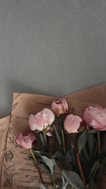 Aesthetic arrangement of pink tulips with green leaves on brown paper over gray surface.