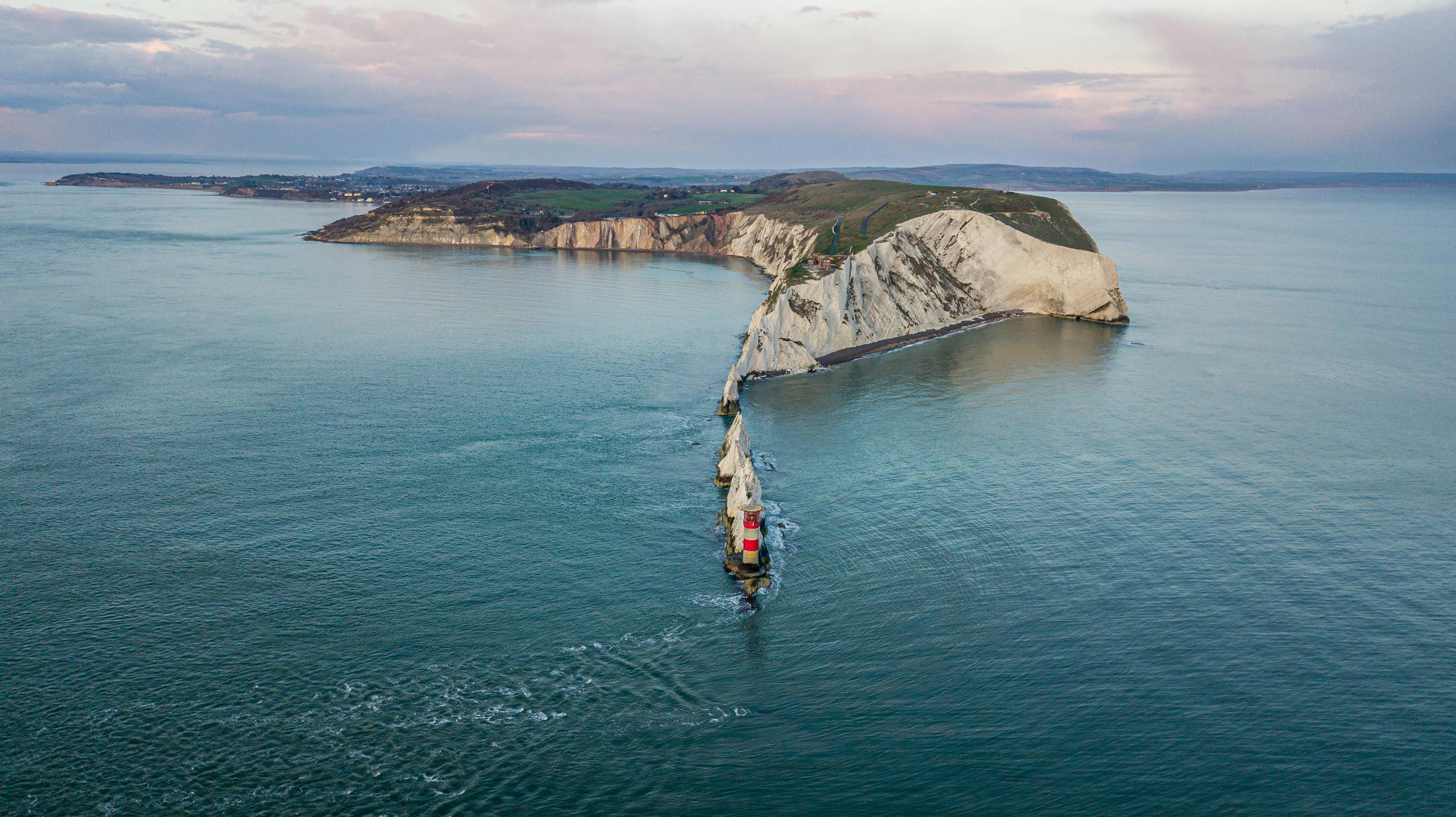 Stunning aerial view of a lighthouse on rugged cliffs extending into the sea under an overcast sky.