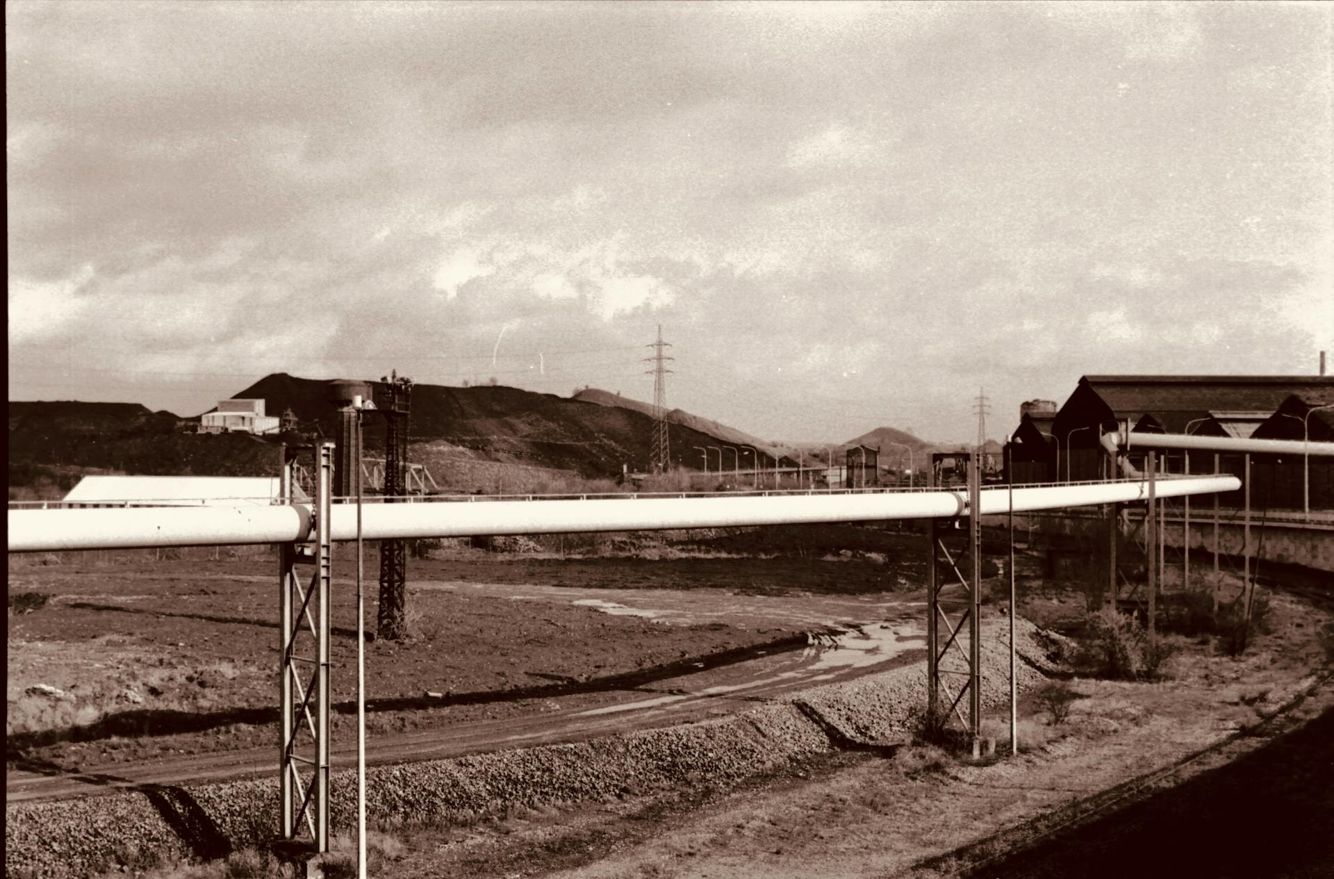 Vintage industrial scene with a large pipeline running through a barren landscape.