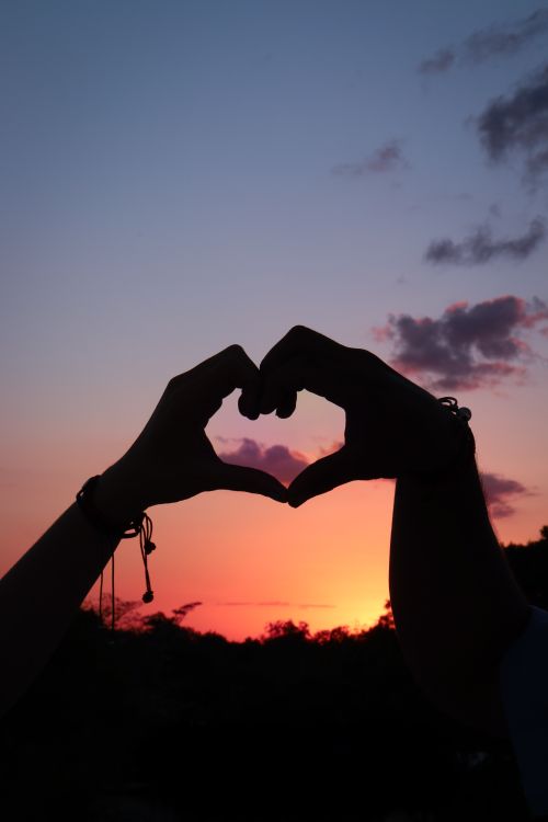 Free Hands form a heart shape against a vibrant sunset sky, symbolizing love and connection. Stock Photo