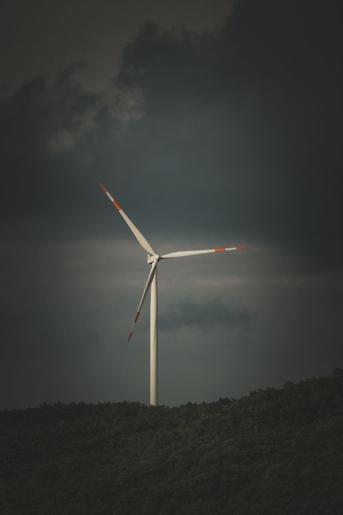 Free Dramatic view of a wind turbine atop a hill against stormy clouds, symbolizing renewable energy. Stock Photo