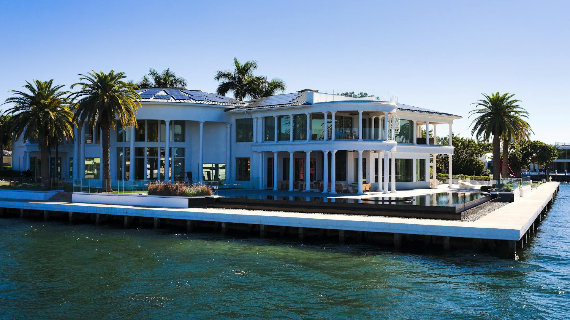 Stunning modern mansion with palm trees by Florida waterfront, perfect for luxury living.