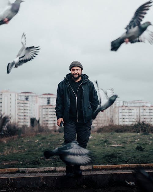 Man Standing in front of Buildings, Pigeons Flying