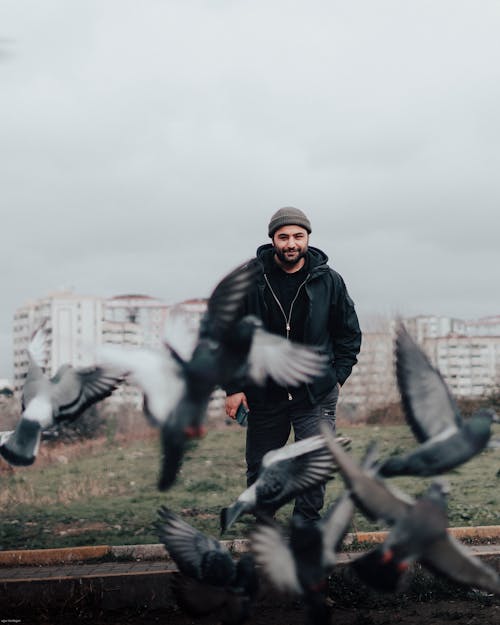 Man Standing in front of Buildings, Pigeons Flying