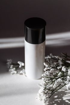 A simple white and black cosmetic bottle adorned with delicate baby's breath flowers, captured in minimalistic style.