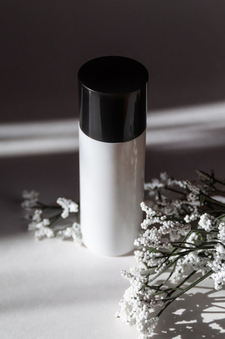 Black And White Makeup Face Cream Bottle Mockup With Spring Flowers And Dramatic Shadows