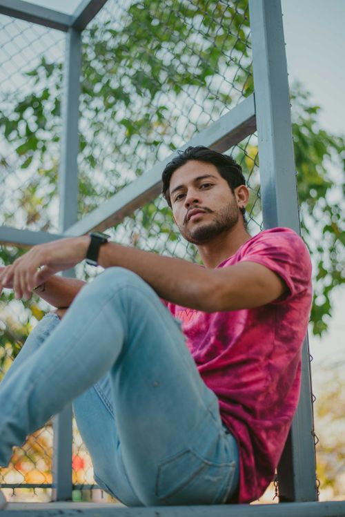 Free A young man in casual attire poses confidently against a metal fence outdoors. Stock Photo