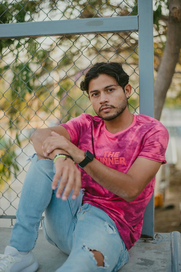 Man Sitting And Leaning On The Metal Fence