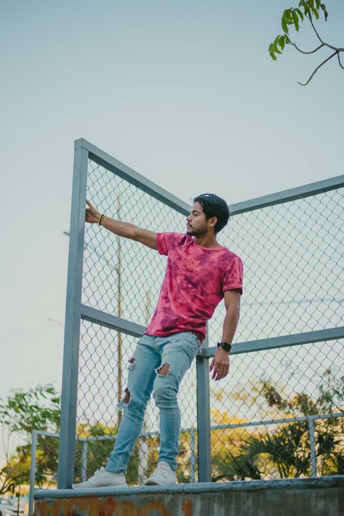 Free Man in pink shirt and ripped jeans leaning on a metal fence. Casual outdoor scene. Stock Photo