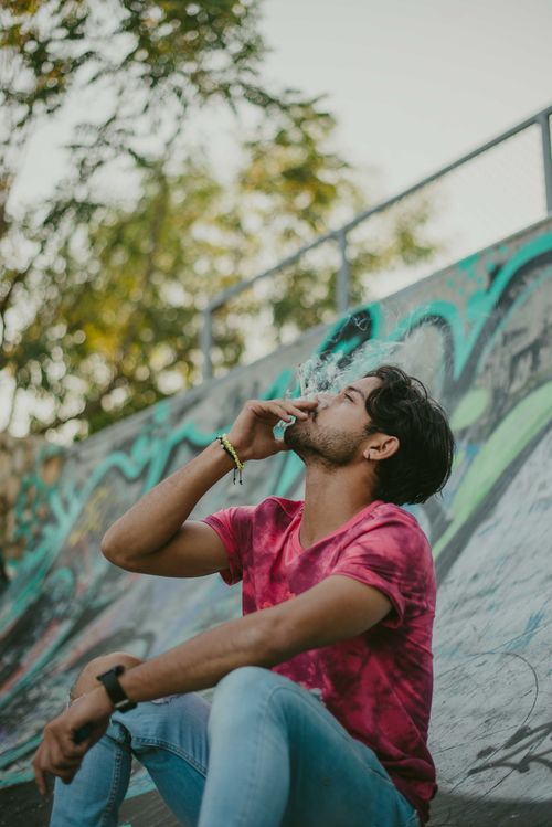 Free A young man sitting at a skate park, smoking with grafitti in the background. Stock Photo