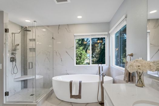 Elegant bathroom featuring a freestanding bathtub and glass shower with natural light and marble accents.