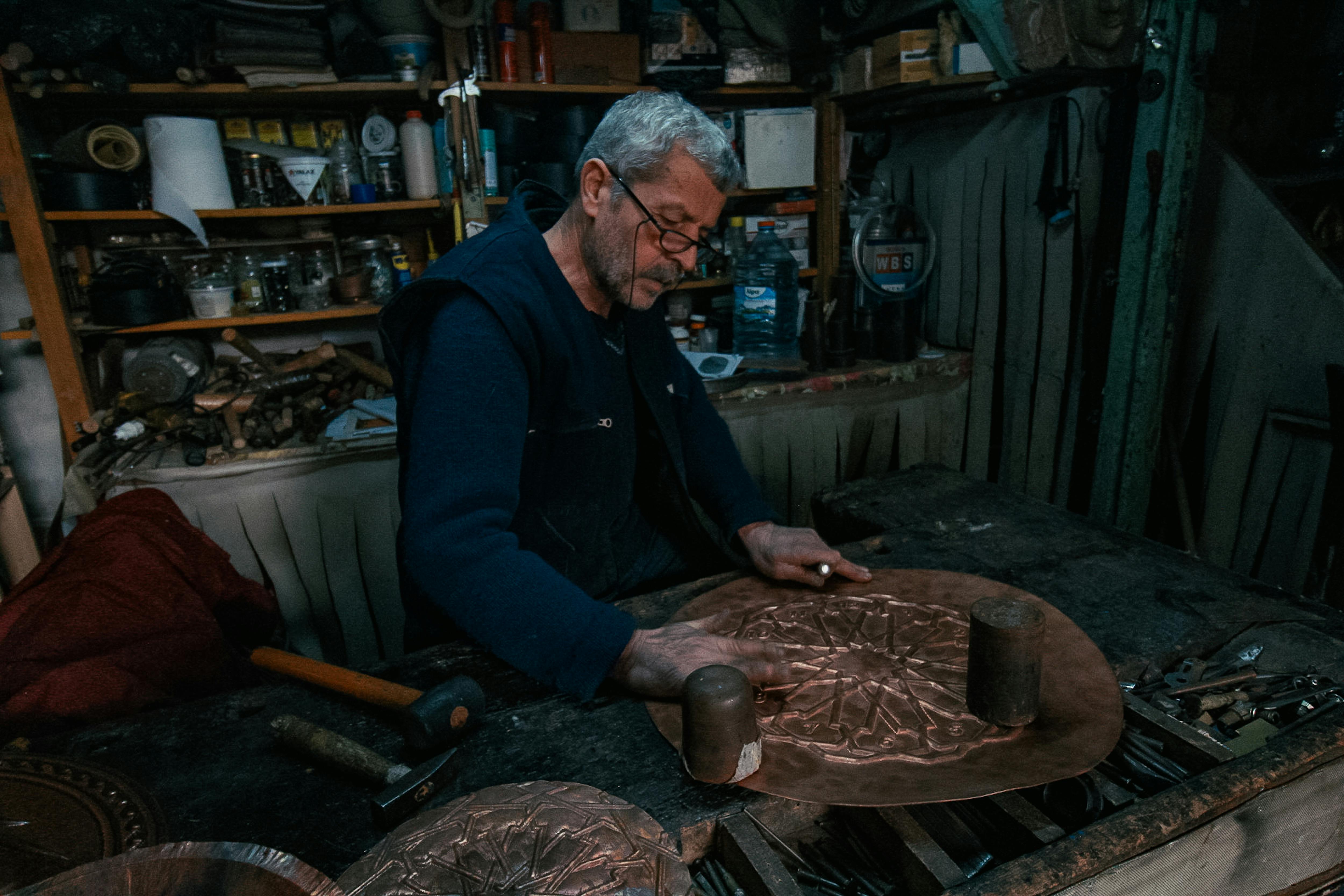 Elderly craftsman working meticulously on copper art in a traditional workshop.